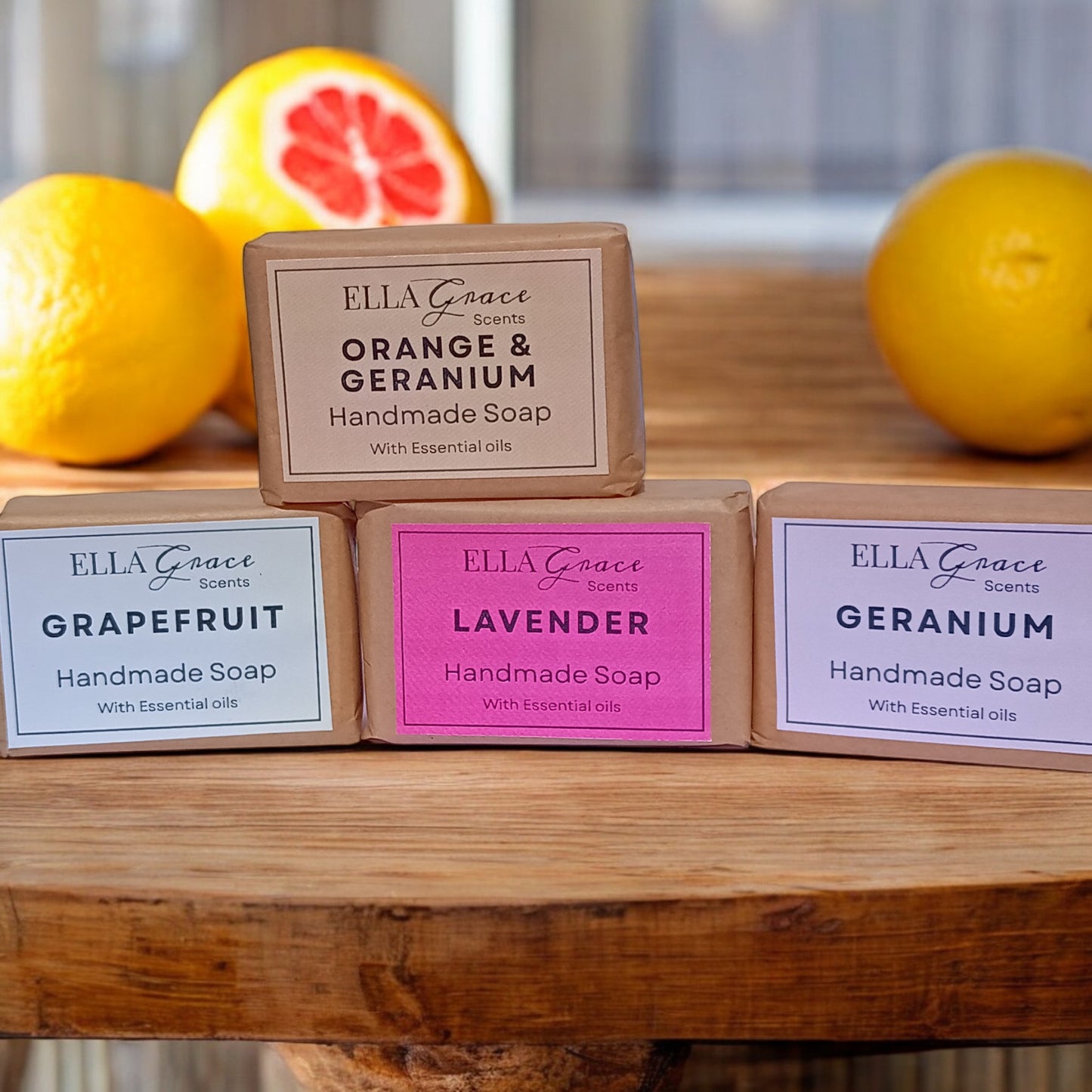 Handmade soap bars from Ella Grace Scents on a wooden surface with lemons and a grapefruit in the background.